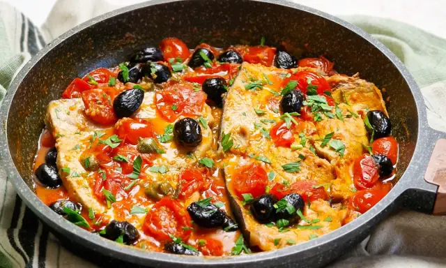 Pesce spada alla siciliana in padella con pomodorini, olive nere e capperi, guarnito con prezzemolo fresco.