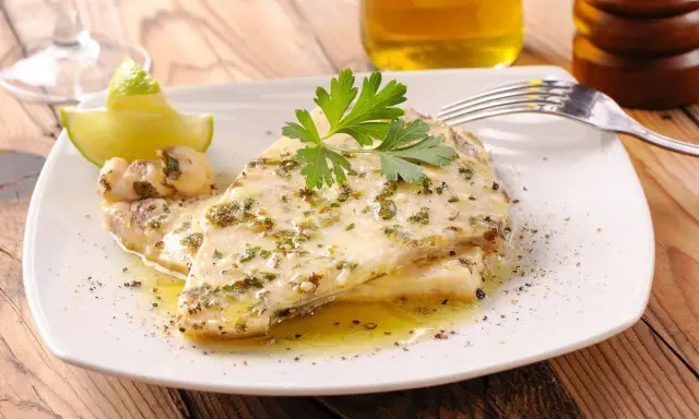 Delizioso pesce spada al forno, condito con erbe aromatiche e servito con spicchi di lime e prezzemolo fresco.