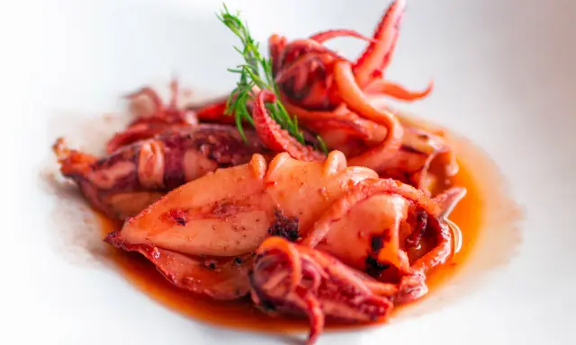 Totani in umido succulenti, cotti lentamente in un sugo saporito, guarniti con un rametto di finocchietto.
