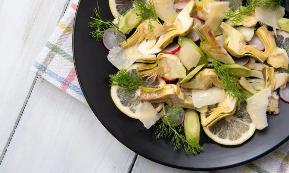 Un'insalata di carciofi crudi, con fette di limone, ravanelli e scaglie di parmigiano, guarnita con aneto fresco.