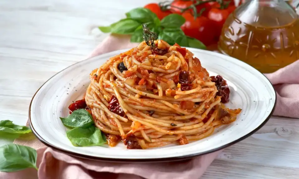 Spaghetti con pomodori secchi, basilico fresco e un filo d'olio d'oliva. Un piatto semplice e gustoso, pronto per essere assaporato.
