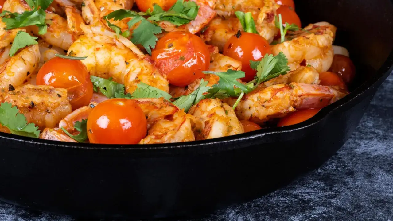 Gamberoni in padella succulenti, cotti con pomodorini e profumati aromi, pronti per essere gustati.