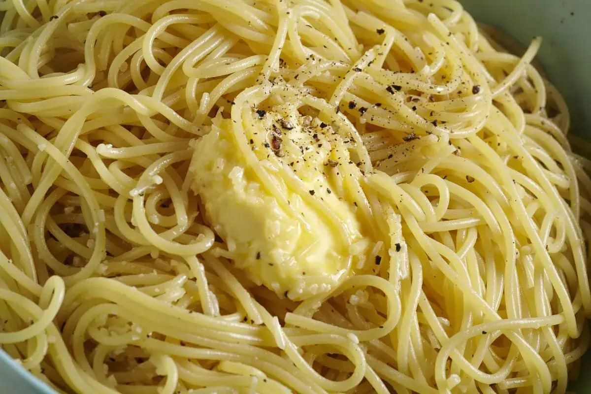 Un piatto di spaghetti fumanti, conditi con burro fuso e pepe nero macinato fresco, un classico cacio e pepe pronto da gustare.