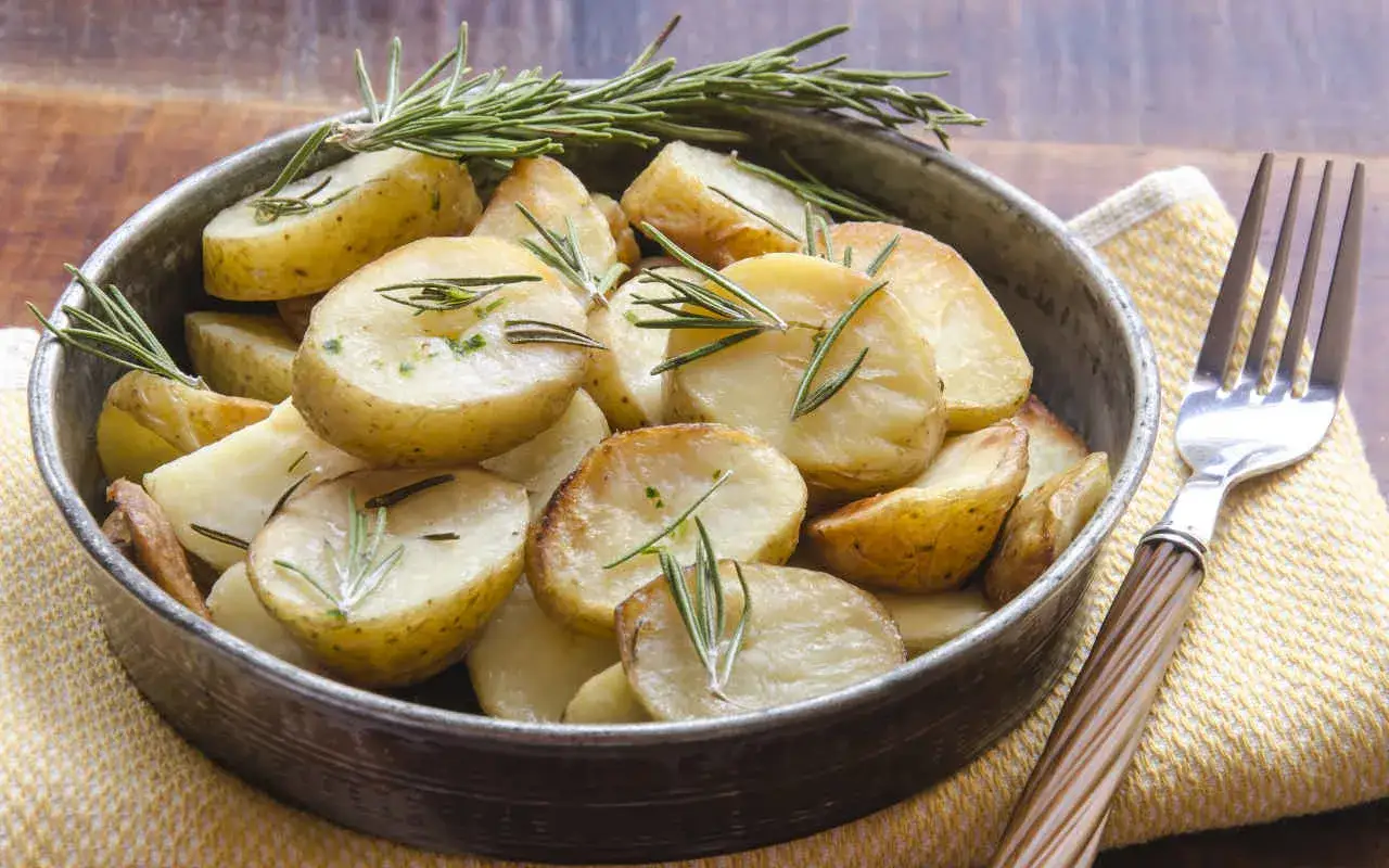 Patate dolci in padella, tagliate a spicchi e profumate al rosmarino, servite in una ciotola di metallo.