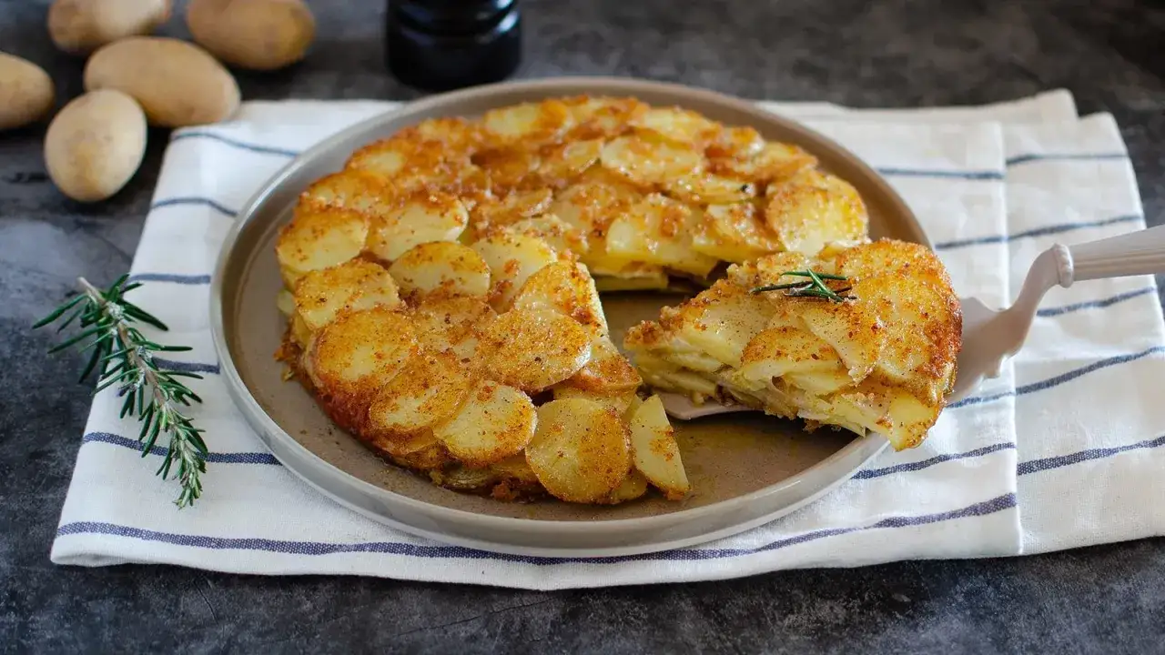 Una fetta di parmigiana di patate dorata e croccante, guarnita con rosmarino, pronta per essere gustata.