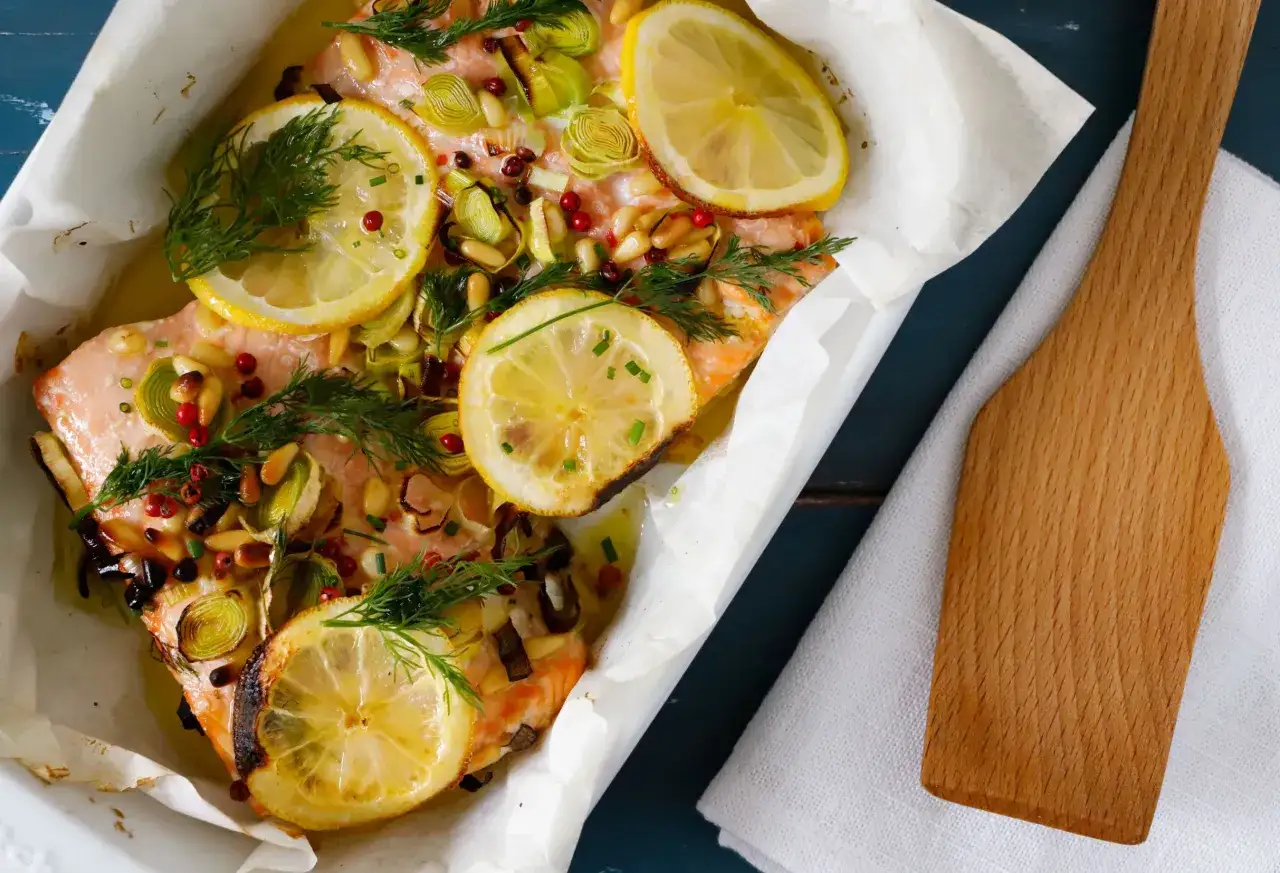 Salmone al forno con limone, erbe aromatiche, pinoli e pepe rosa. Un piatto succulento e profumato, pronto per essere gustato.