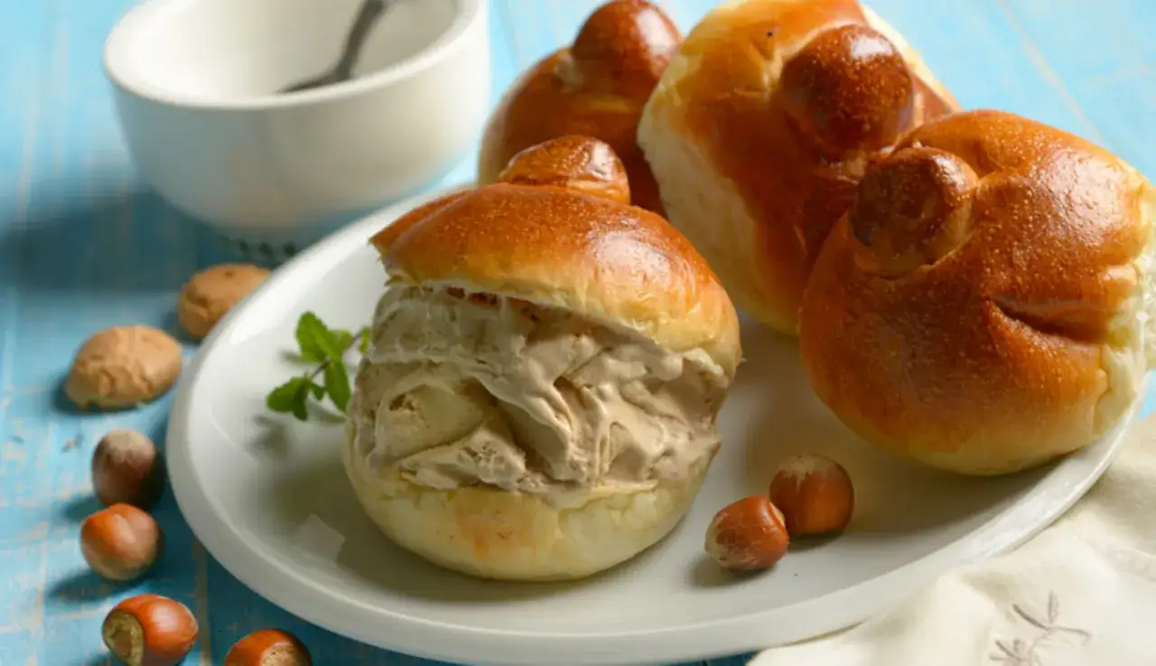 Brioche col tuppo ripiena di gelato, con nocciole e menta su piatto bianco.