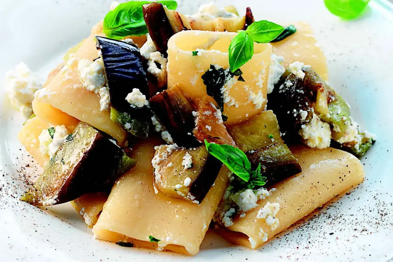 Un piatto invitante di pasta con melanzane, ricotta fresca e basilico, condito con pepe nero macinato.
