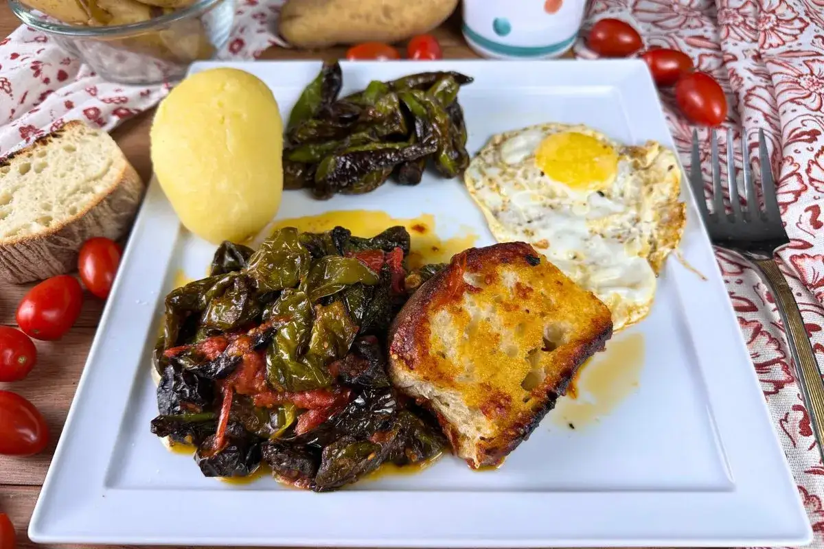 Piatto con friggitelli in padella, uovo fritto, patata lessa e pane tostato. Un pasto semplice e gustoso.