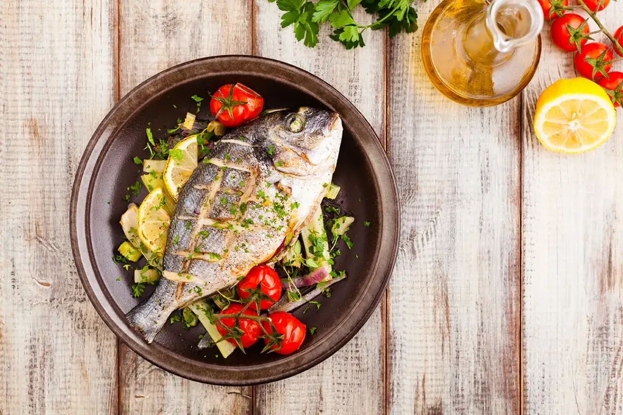 Un delizioso pesce alla brace, guarnito con pomodorini e limone, pronto per essere gustato.