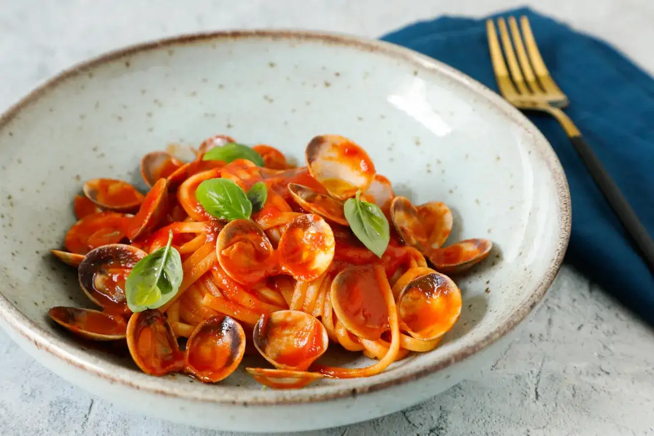 Spaghetti alle vongole surgelate, un piatto gustoso e veloce. Pasta con vongole e pomodoro, guarnito con basilico fresco.