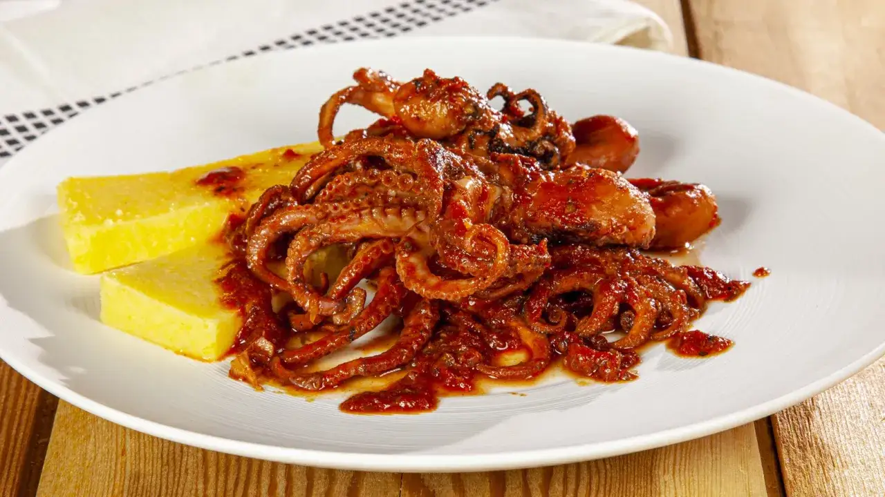 Polipetti in purgatorio, un piatto succulento con tentacoli avvolti in salsa rossa piccante, serviti su polenta dorata.