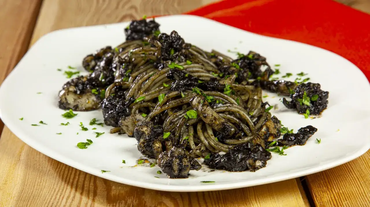 Un piatto invitante di spaghetti al nero di seppia, guarnito con prezzemolo fresco, su un piatto bianco.