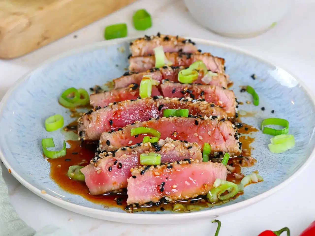 Fette di tataki di tonno scottato, ricoperte di semi di sesamo, guarnite con cipollotto fresco e salsa agrodolce.