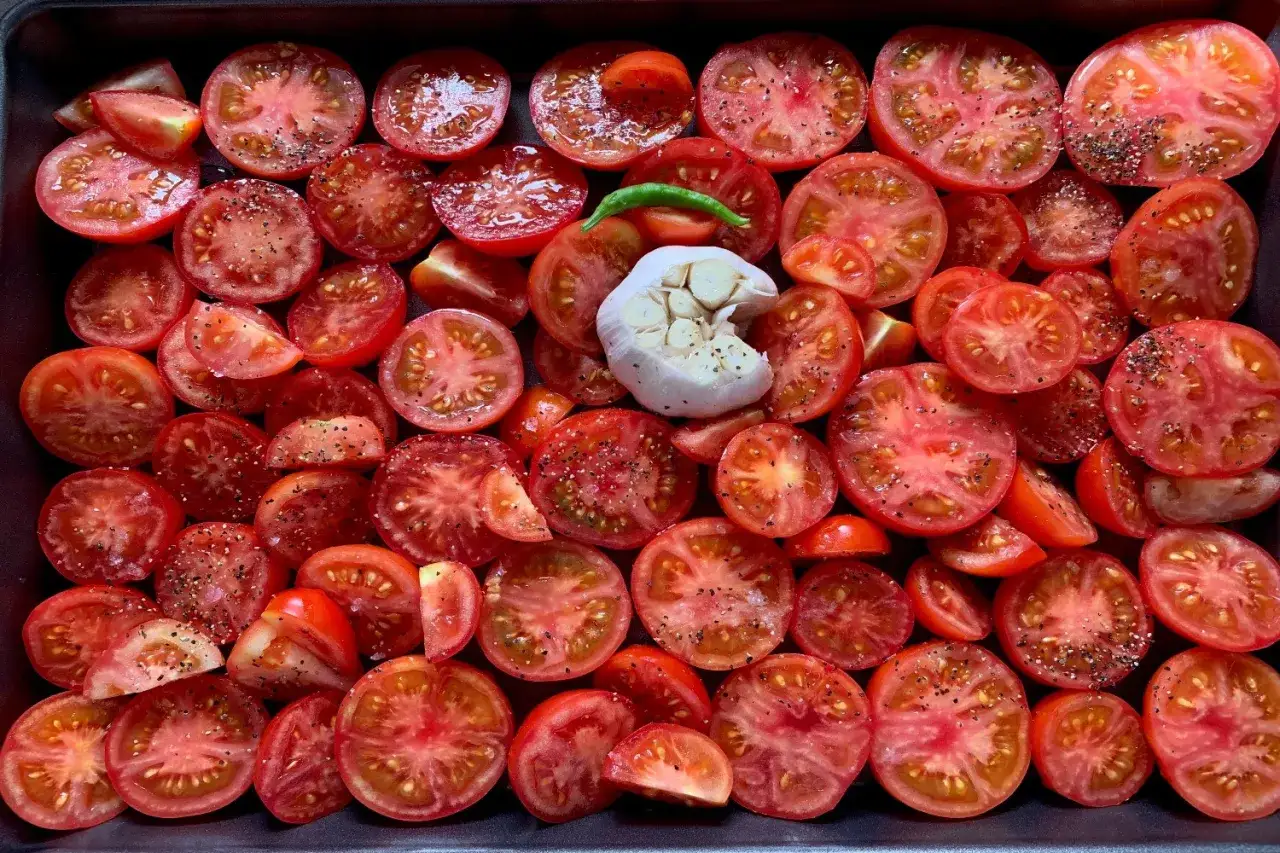 Pomodorini al forno pronti per essere cotti, conditi con aglio e peperoncino.