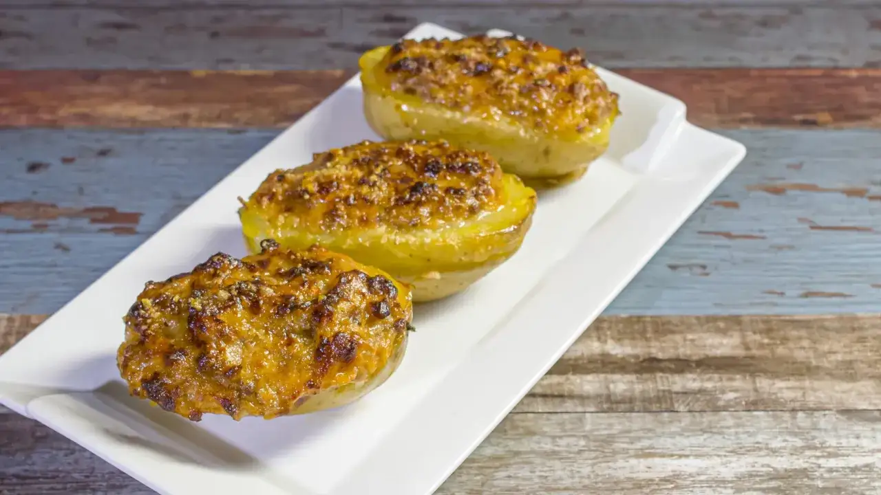 Tre patate ripiene al forno, dorate e croccanti, servite su un piatto bianco.