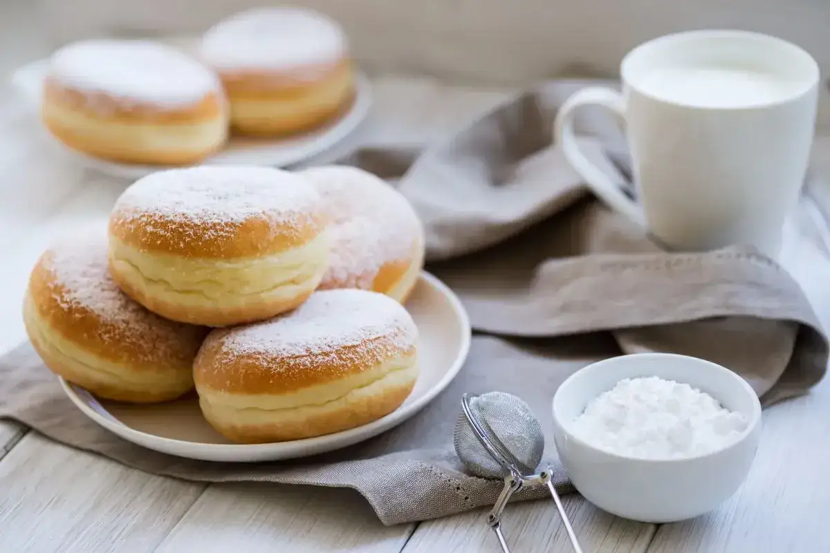 Bomboloni ricetta originale: soffici e dorati, spolverati di zucchero a velo, pronti per essere gustati con un bicchiere di latte.