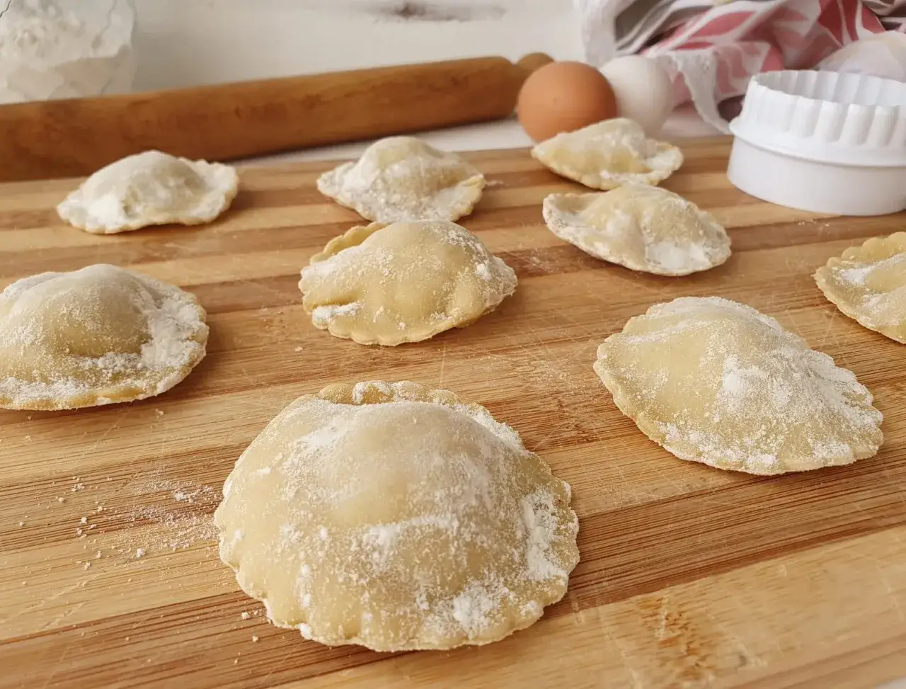 Ravioli di carne fatti in casa, pronti per essere cotti, spolverati di farina su un tagliere di legno.