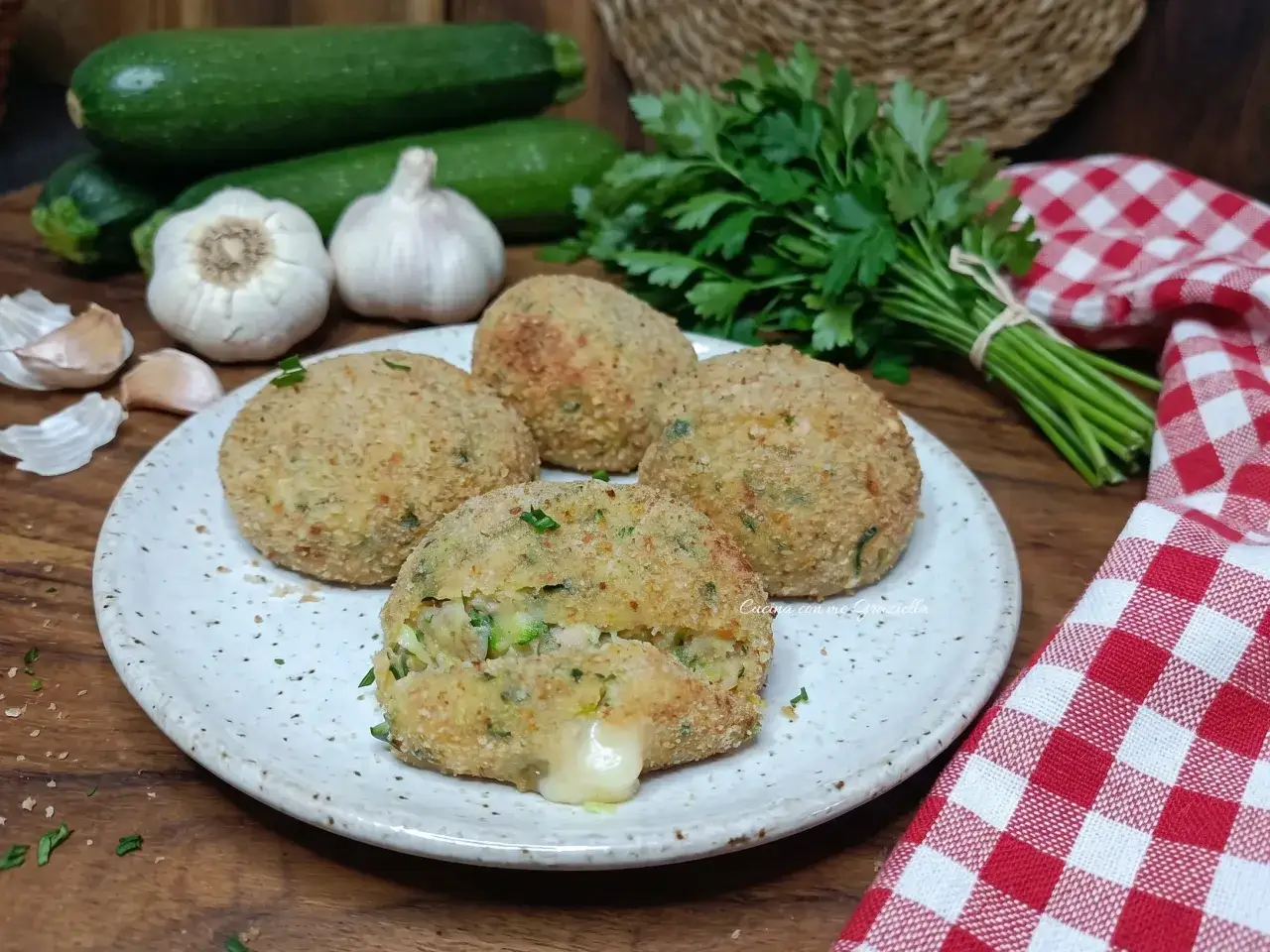 Polpette di zucchine e tonno dorate e croccanti, con un cuore filante di formaggio. Ingredienti freschi come zucchine, aglio e prezzemolo sullo sfondo.