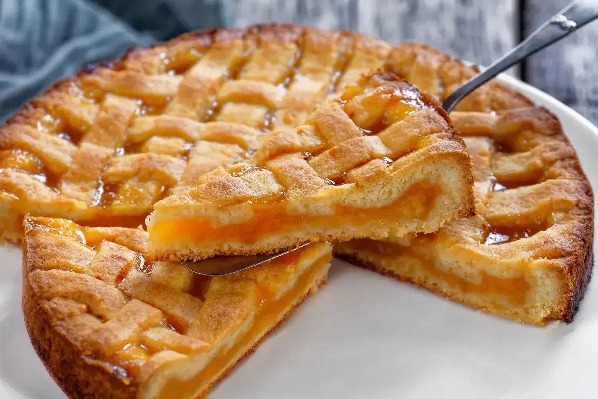 Deliziosa crostata senza glutine con ripieno di albicocche, una fetta sollevata mostra la sua morbidezza.