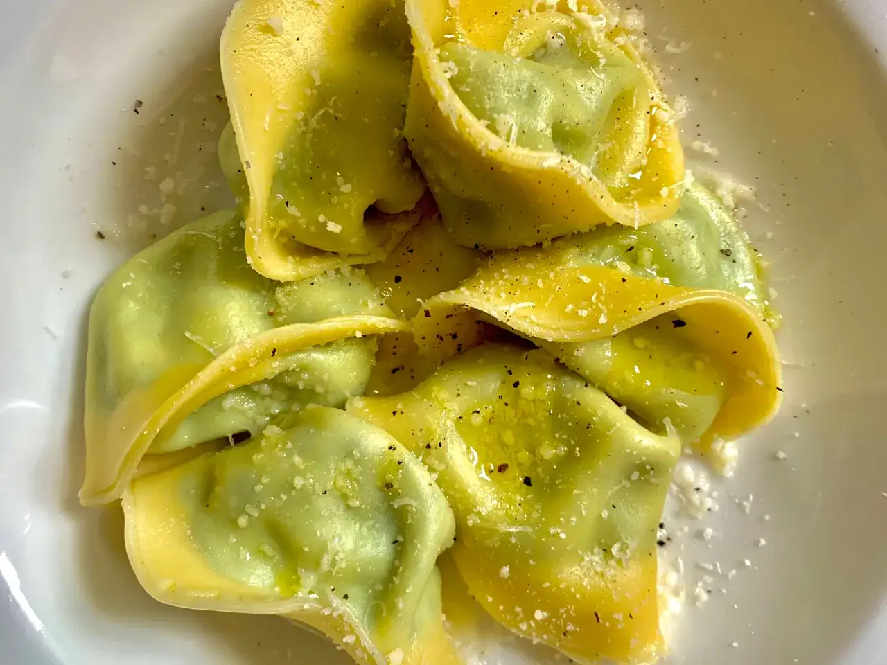 Ravioli fatti in casa, verdi e gialli, conditi con olio, pepe e parmigiano. Un piatto invitante che profuma di tradizione.