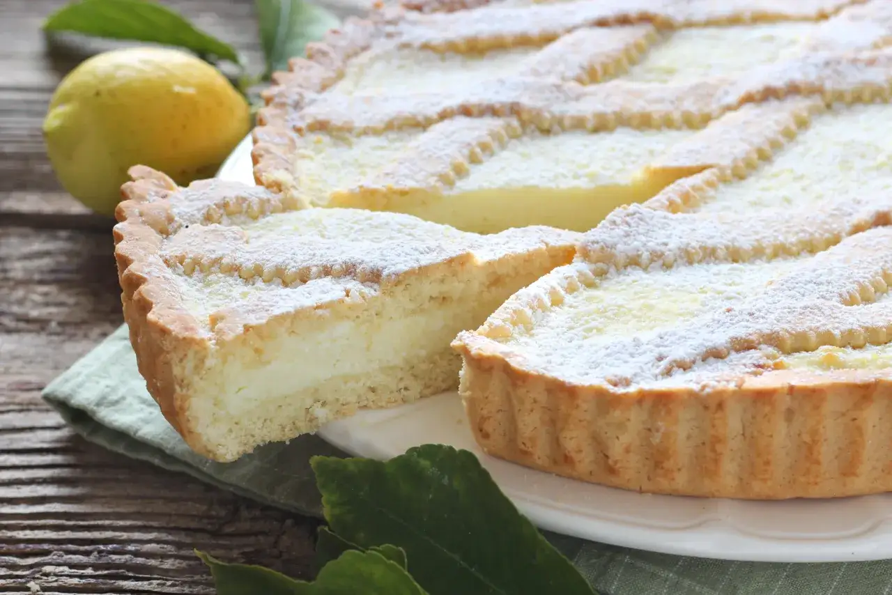 Una fetta di crostata di ricotta, cosparsa di zucchero a velo, accanto a un limone su un tavolo di legno.