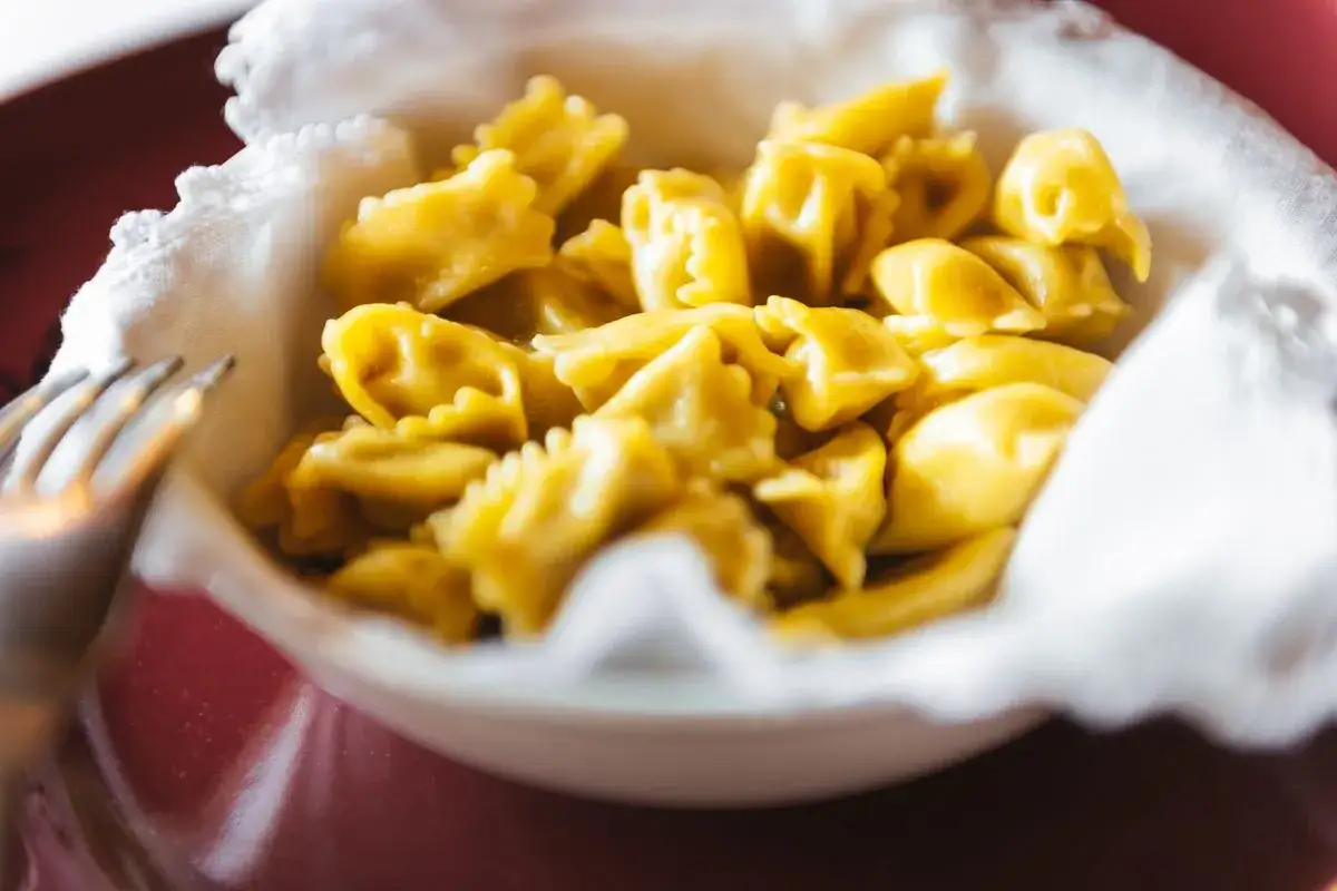 Un primo piatto invitante: tanti ravioli del plin dorati, serviti in una ciotola bordata di bianco.