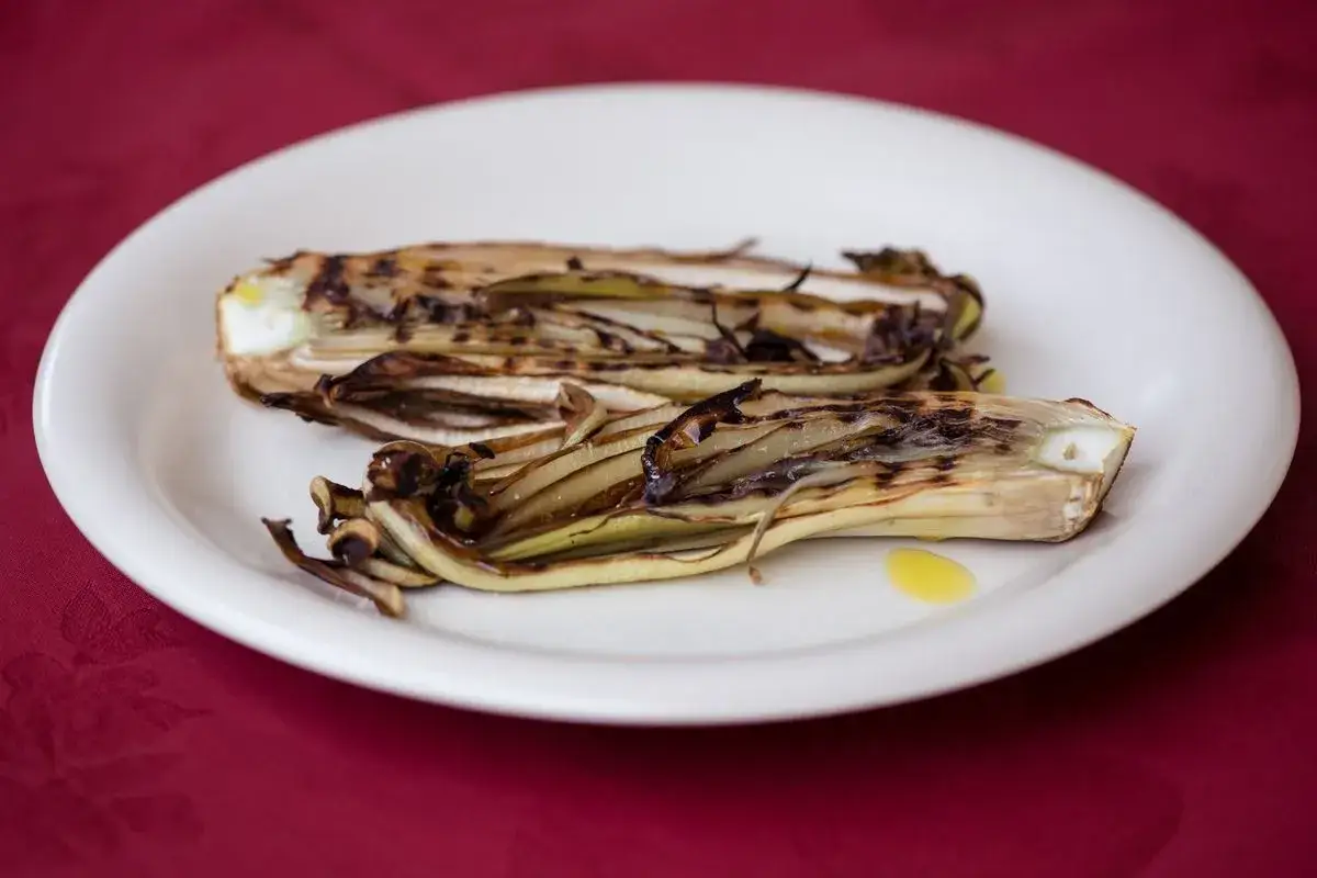 Radicchio in padella, grigliato e caramellato, servito su un piatto bianco con un filo d'olio.