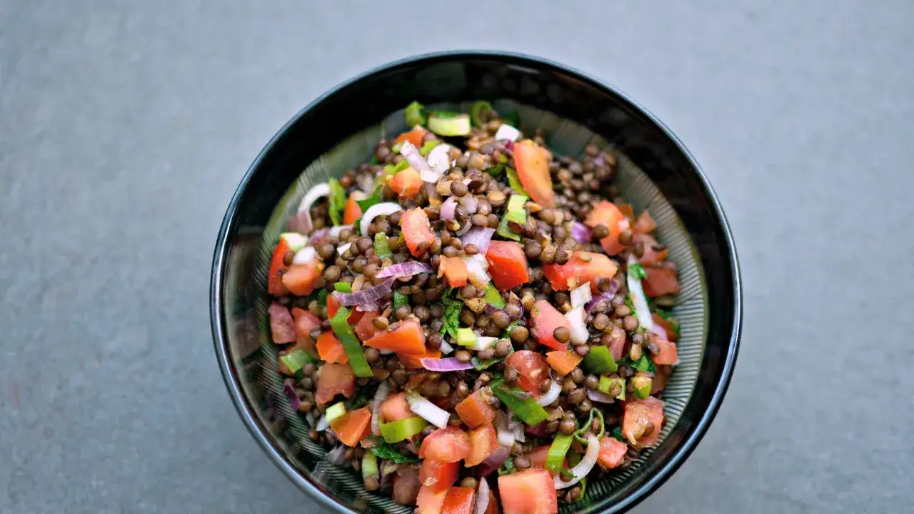 Una ciotola di colorata insalata di lenticchie con pomodori, cipolla rossa e erbe fresche.