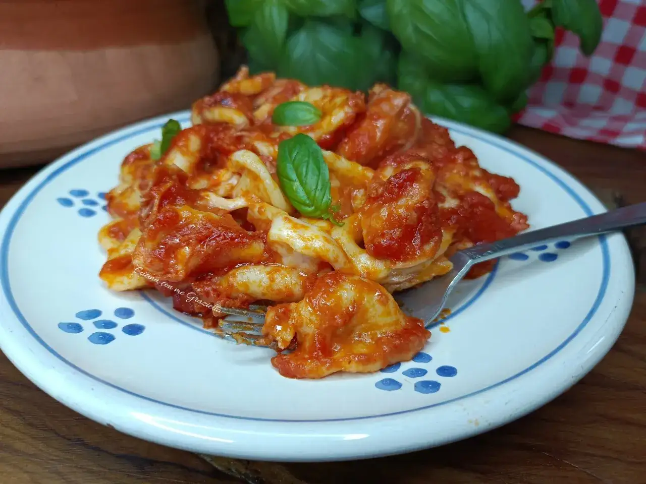 Orecchiette al forno con sugo rosso e basilico fresco, servite su un piatto decorato.