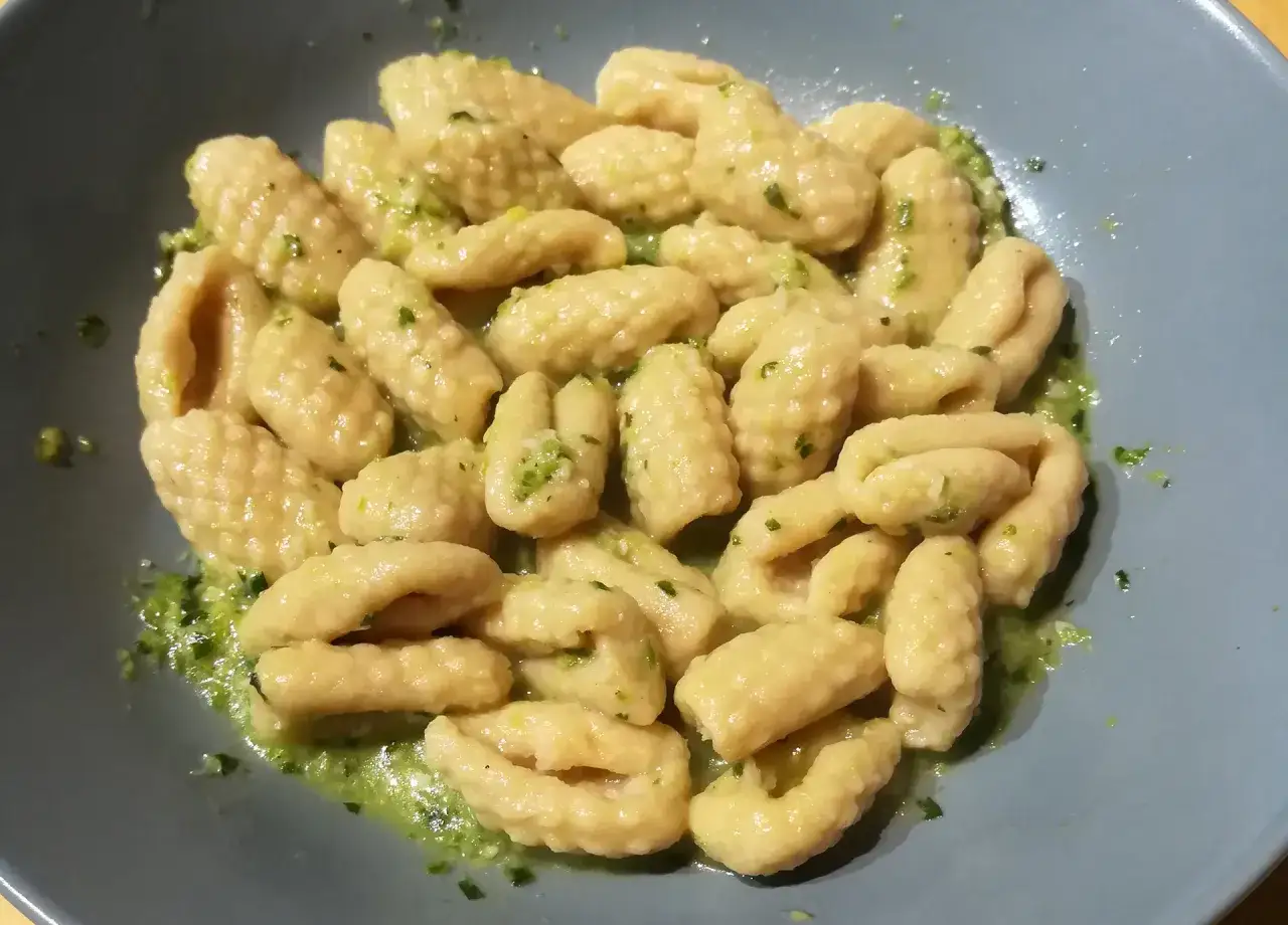 Gnocchi di ceci conditi con un pesto verde brillante, serviti in un piatto grigio.