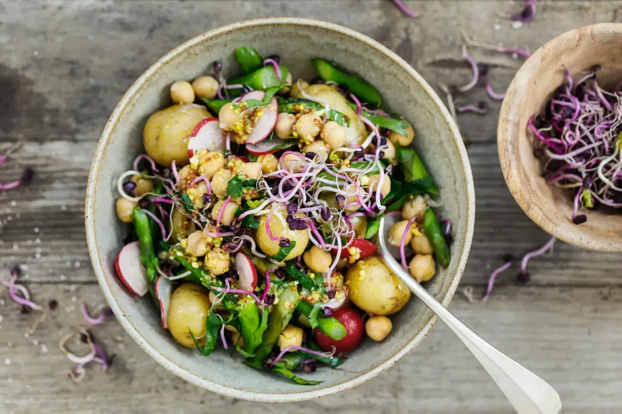 Deliziosa insalata di patate con ceci, ravanelli, germogli viola e verdure fresche, condita con una vinaigrette ai semi di senape.