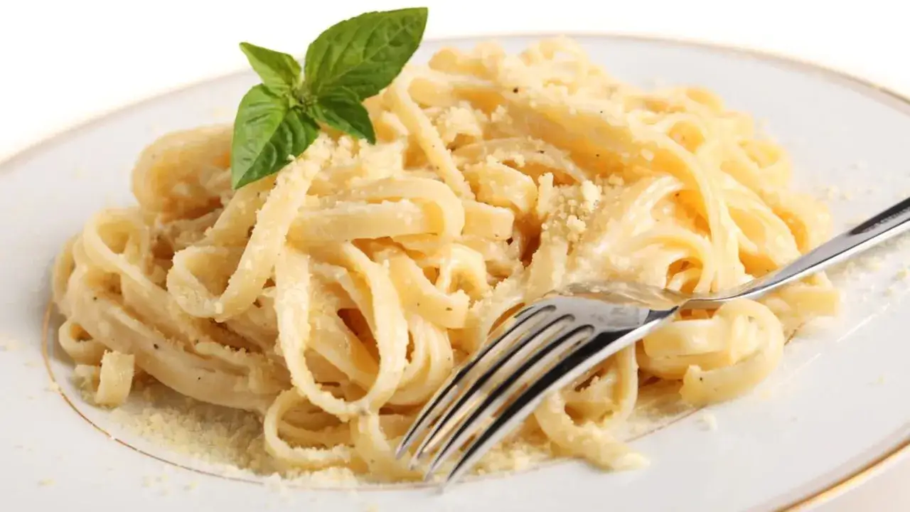 Un piatto di pasta in bianco, condita con formaggio grattugiato e guarnita con una fogliolina di basilico. Una forchetta &egrave; appoggiata sul piatto.