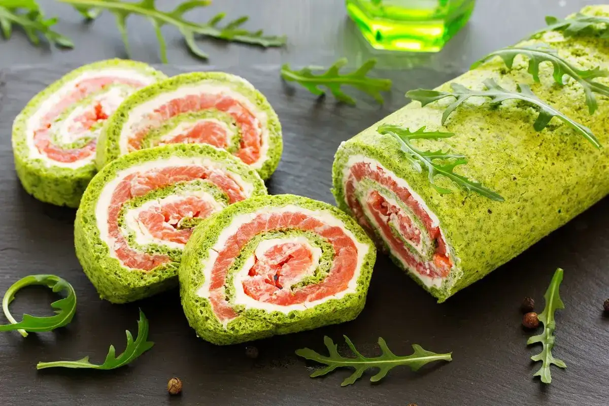 Rotolo di frittata verde con salmone e formaggio cremoso, guarnito con rucola. Un antipasto colorato e gustoso.