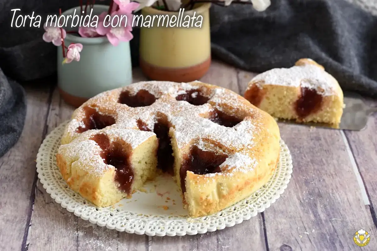 Torta morbida con marmellata, cosparsa di zucchero a velo, su un piatto bianco. Una fetta è già stata servita.