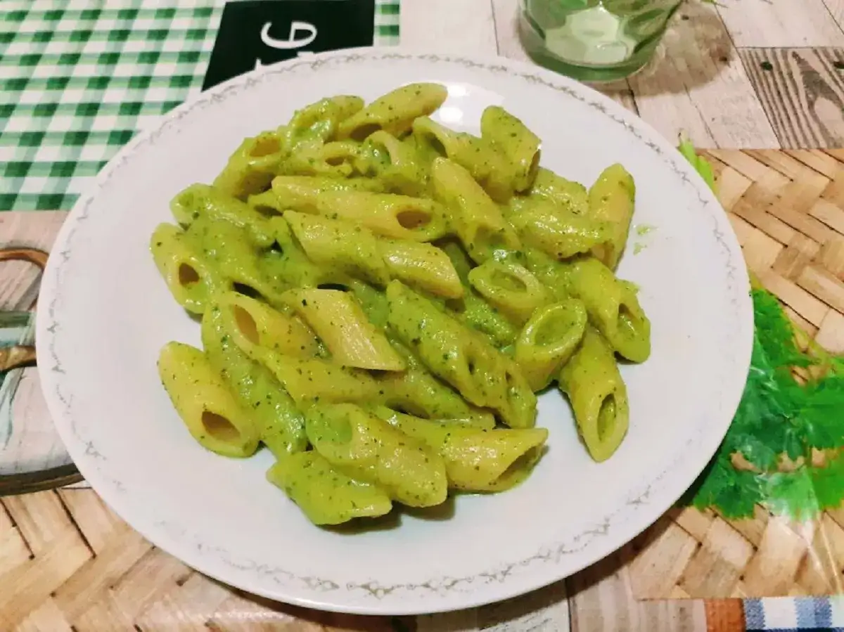 Piatto di penne condite con una cremosa salsa verde, un'invitante pasta con crema di zucchine, guarnita con erbe fresche.