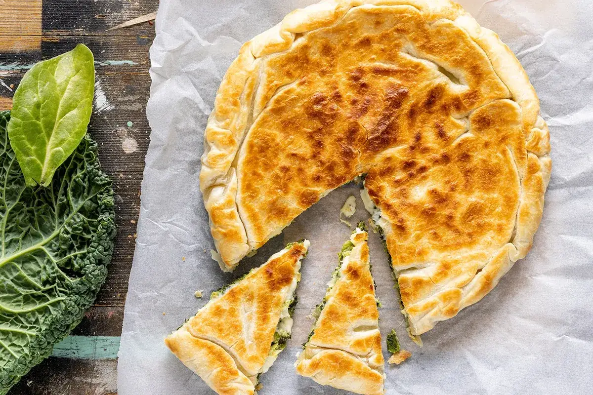 Torta salata dorata, ripiena di verdure, perfetta per torte salate velocissime. Accanto, foglie di cavolo.