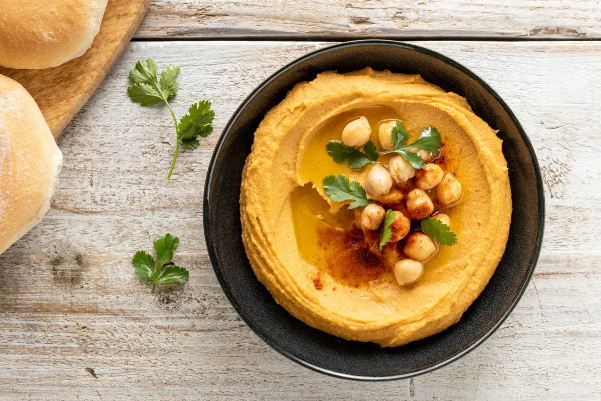 Cremoso hummus di ceci, guarnito con ceci interi, prezzemolo e paprika, pronto per essere gustato con pane.