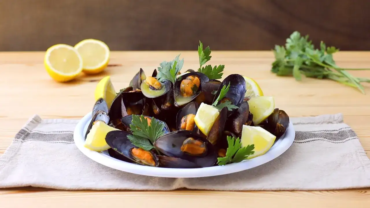 Un piatto fumante di impepata di cozze, guarnito con spicchi di limone e prezzemolo fresco, pronto per essere gustato.