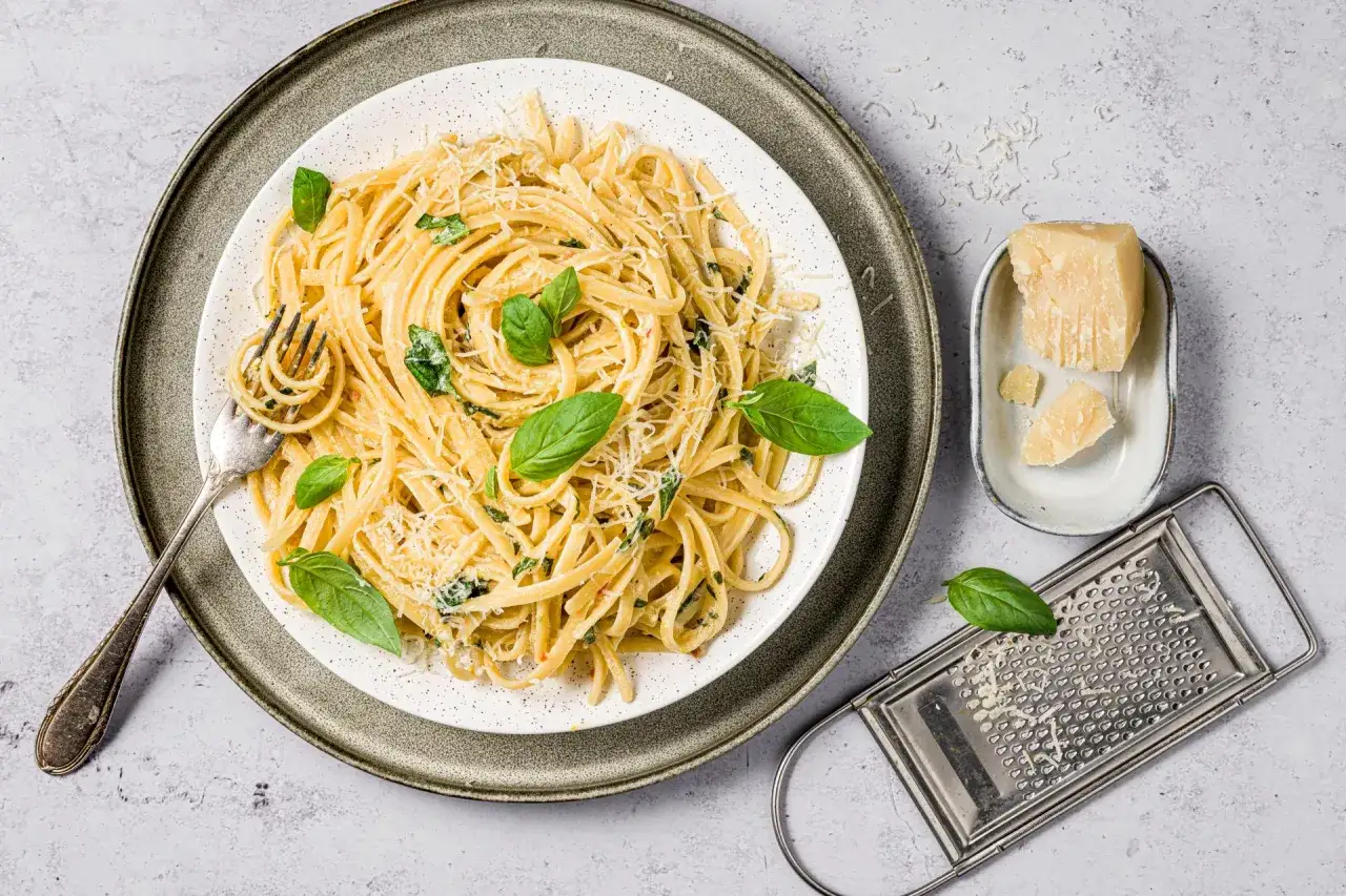 Un piatto di spaghetti al limone, guarnito con basilico fresco e parmigiano grattugiato, pronto per essere gustato.