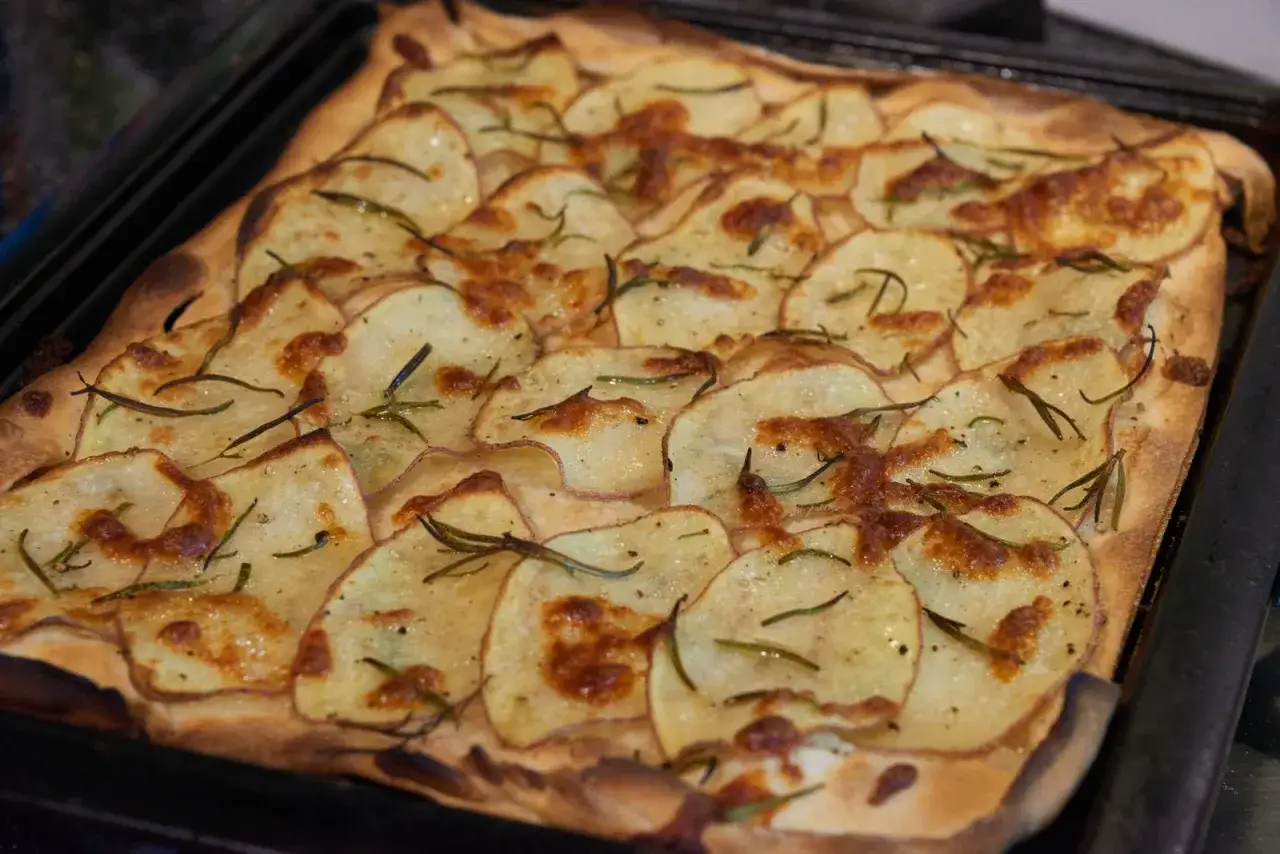 Schiacciata di patate croccante, dorata e profumata al rosmarino, appena sfornata su una teglia.