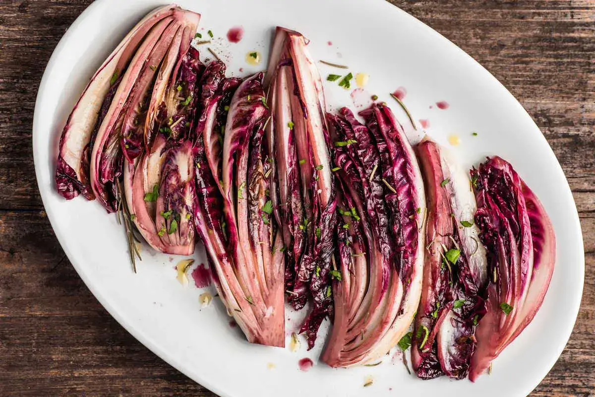 Radicchio al forno, tagliato a spicchi e condito con erbe aromatiche, servito su un piatto bianco.