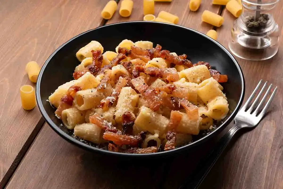 Un piatto fumante di pasta alla zozzona, con rigatoni conditi con guanciale croccante, pecorino e pepe nero.