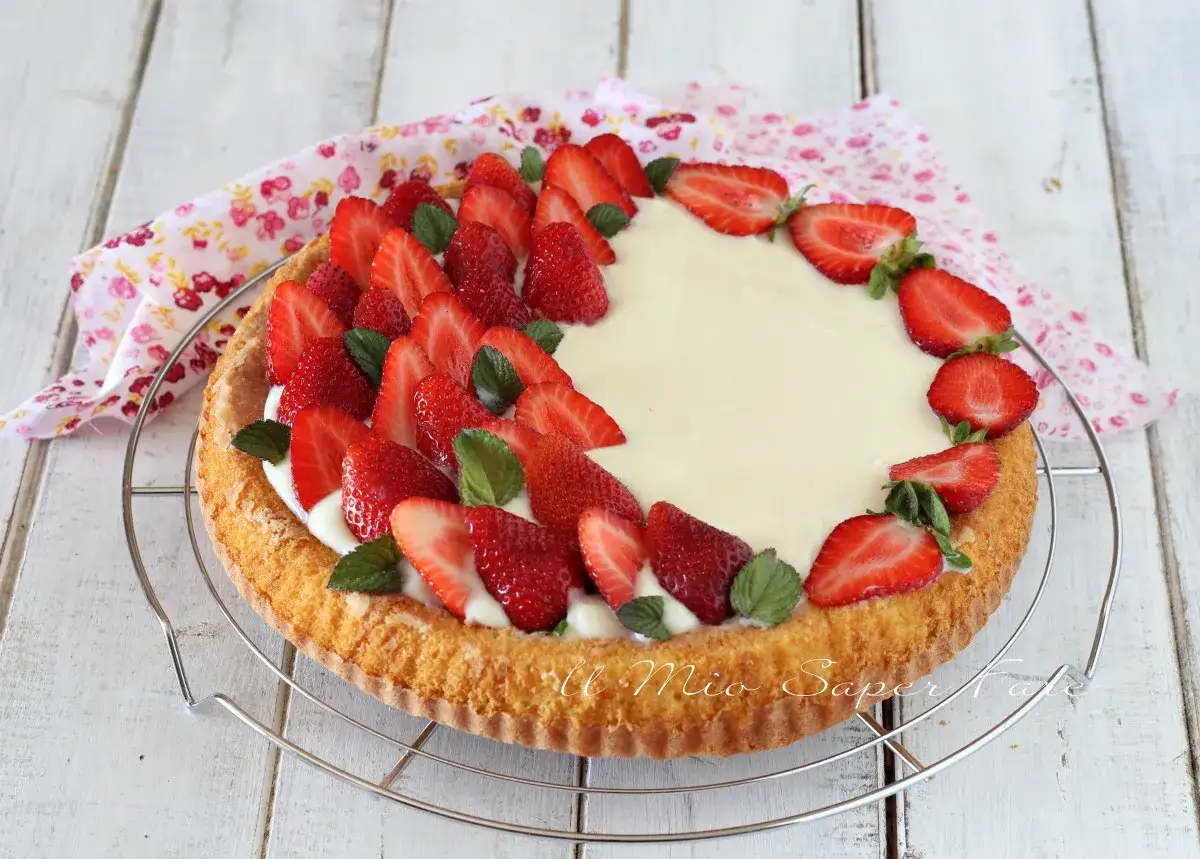 Una deliziosa crostata morbida alle fragole, con crema pasticcera e fragole fresche, decorata con foglioline di menta.