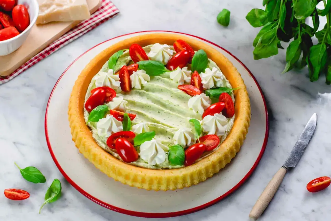 Crostata morbida salata con crema verde, pomodorini e ciuffetti di panna. Fresca e invitante, perfetta per un aperitivo.