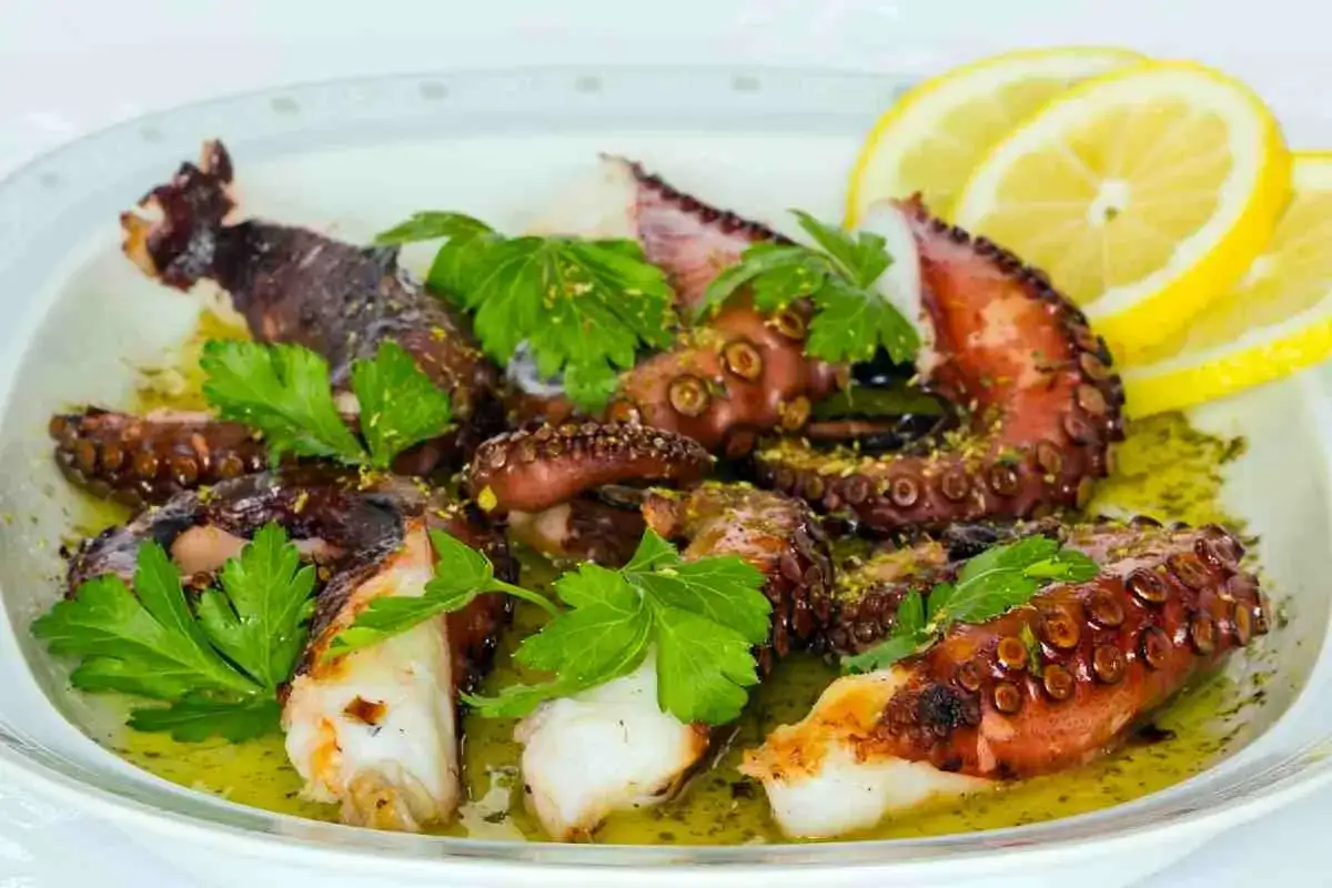 Tentacoli di polpo alla griglia succulenti, conditi con olio, prezzemolo e scorza di limone, serviti con spicchi di limone fresco.