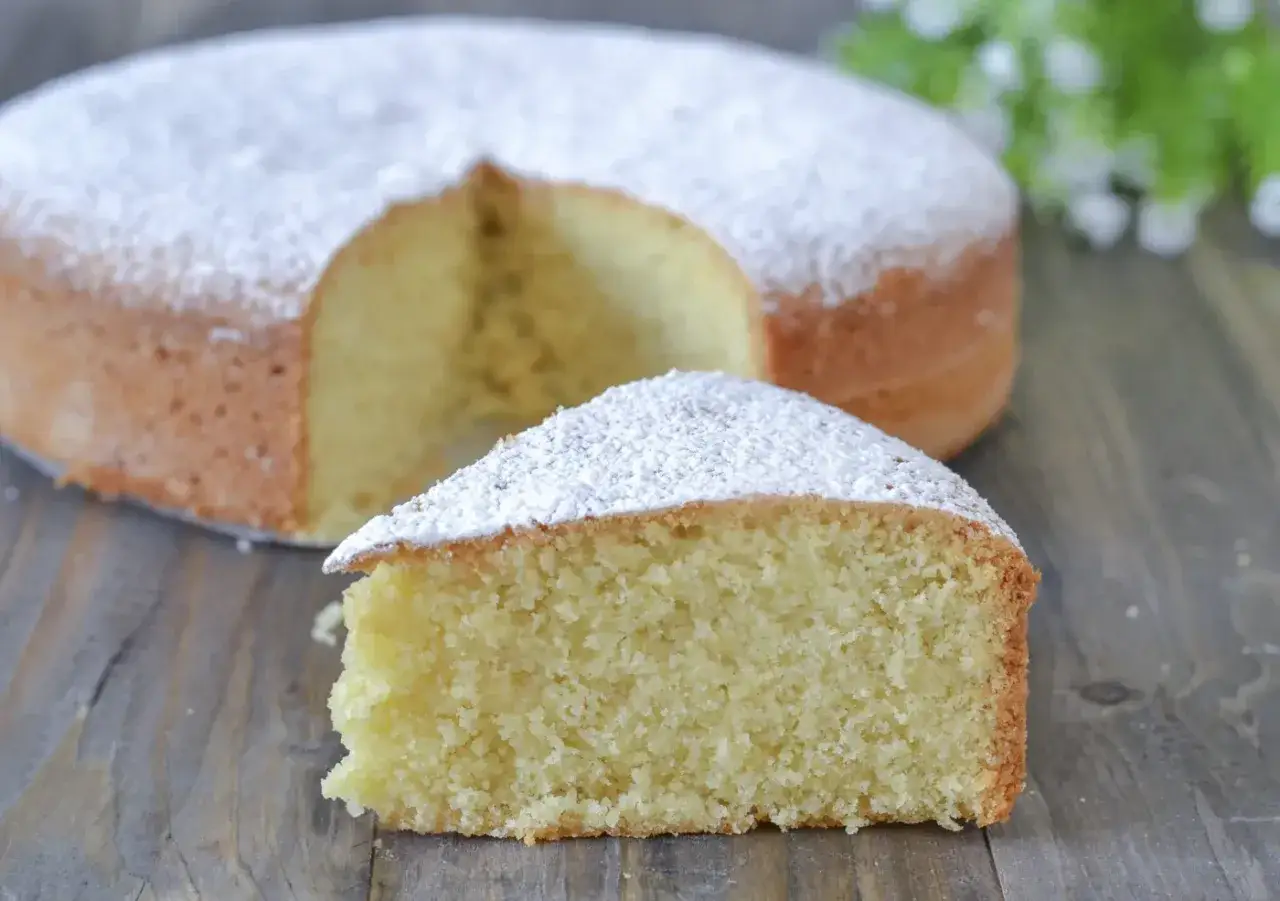 Una fetta di torta con farina di mandorle, cosparsa di zucchero a velo, su un tavolo di legno.