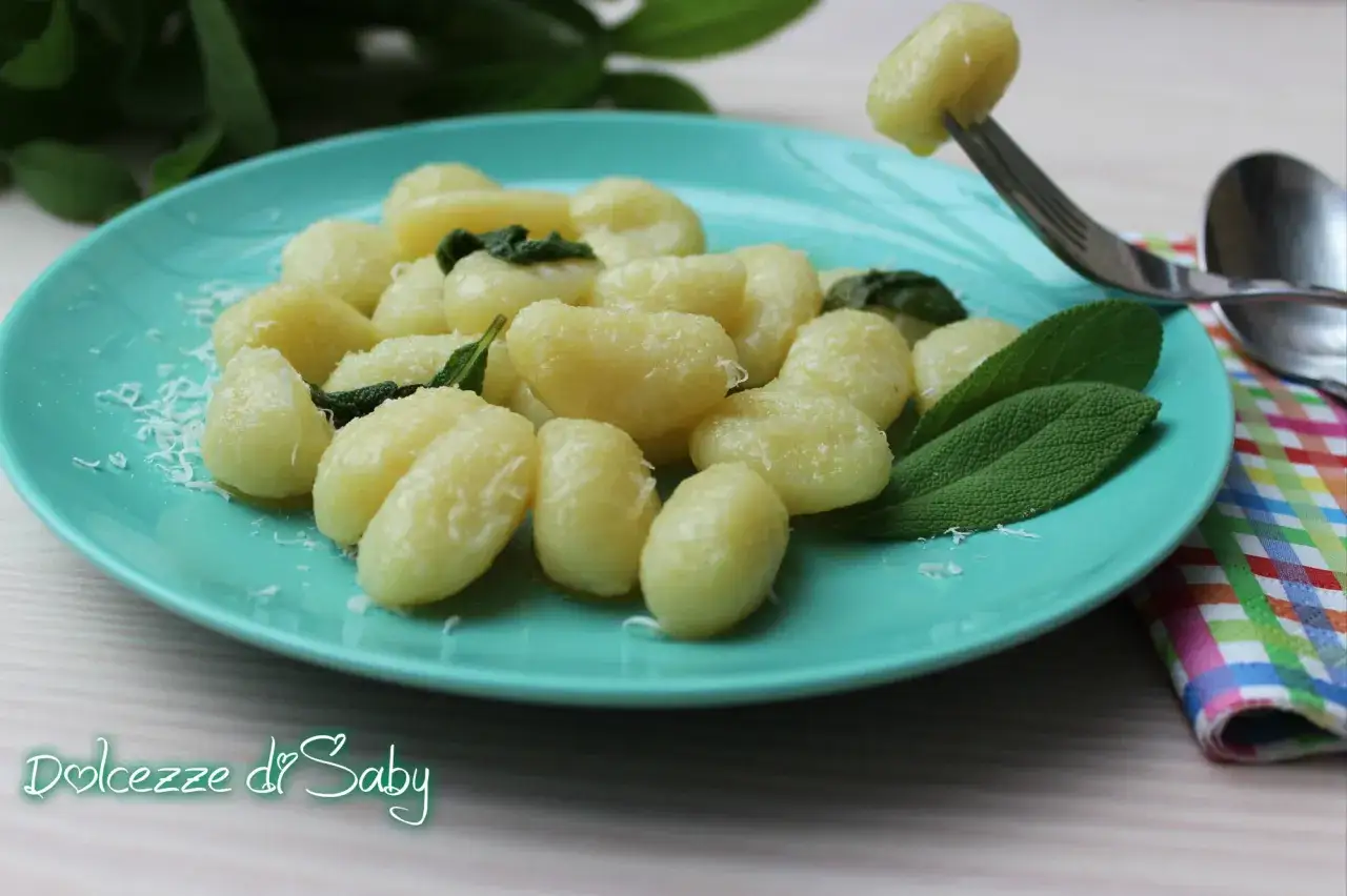 Gnocchi di ricotta soffici su piatto turchese, conditi con parmigiano e foglie di salvia fresca. Un boccone delizioso!
