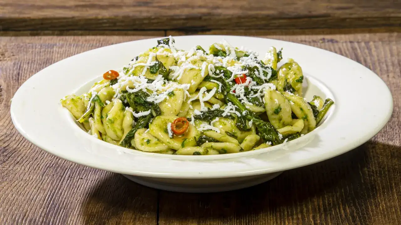 Piatto di orecchiette cime di rapa, condite con verdure verdi, peperoncino e formaggio grattugiato, servite su un piatto bianco.