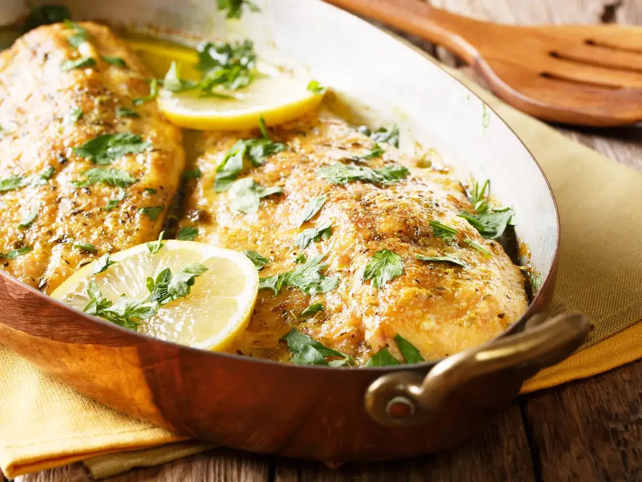 Trota salmonata al forno, dorata e succulenta, guarnita con fette di limone e prezzemolo fresco in una teglia di rame.